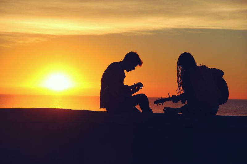 Un baiat si o fata adolescenti pe maulul marii la apus canta la chitara