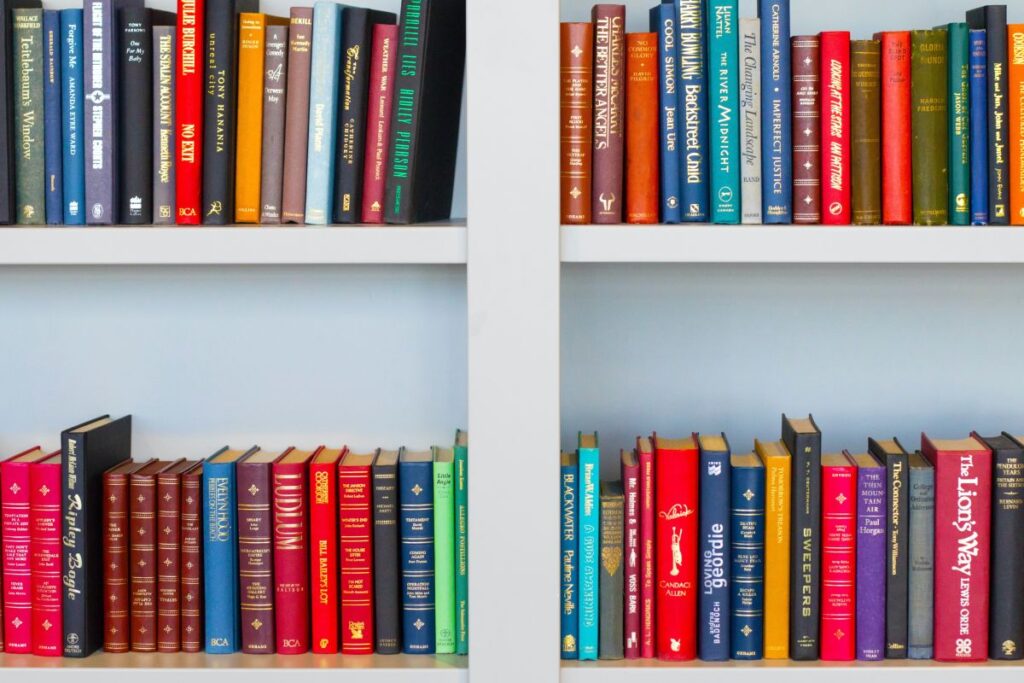 4 rafturi de carti multicolore in engleza intr-o biblioteca alba