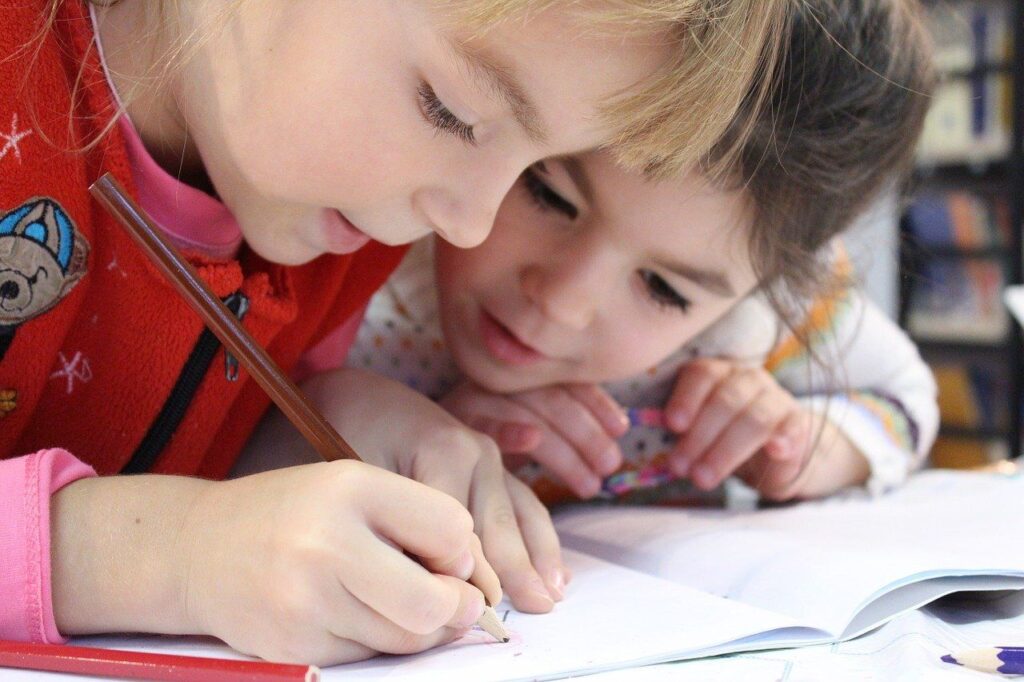fetite de varsta scolara aplecate deasupra unui birou scriu pe un caiet propozitii in engleza