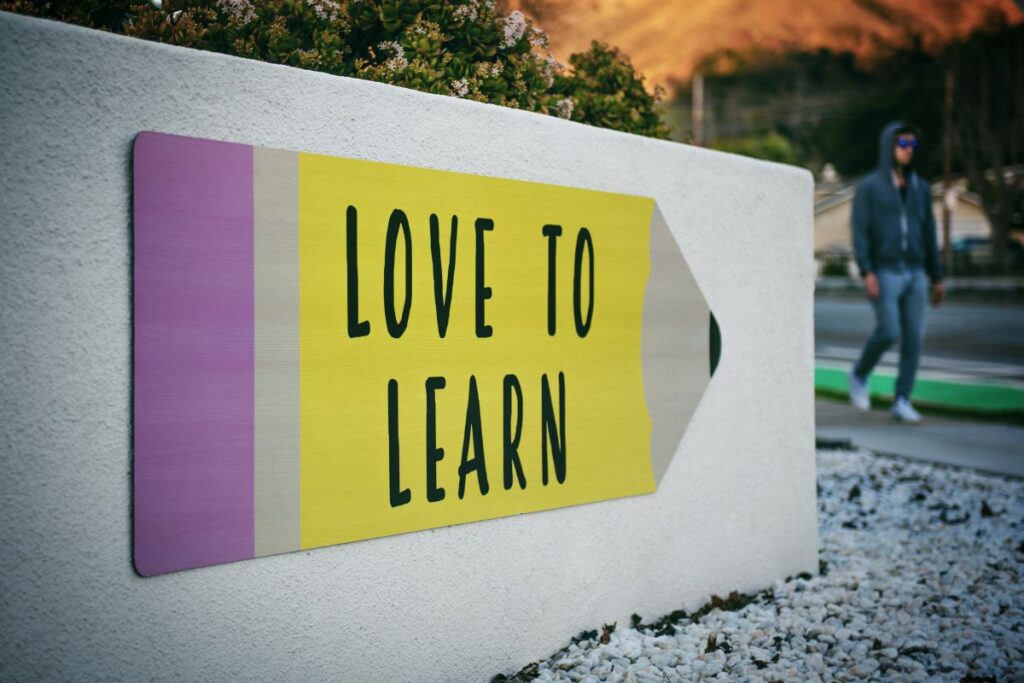 panou de ciment pe care e desenată cu galben și mov o săgeată pe care scrie Love to learn