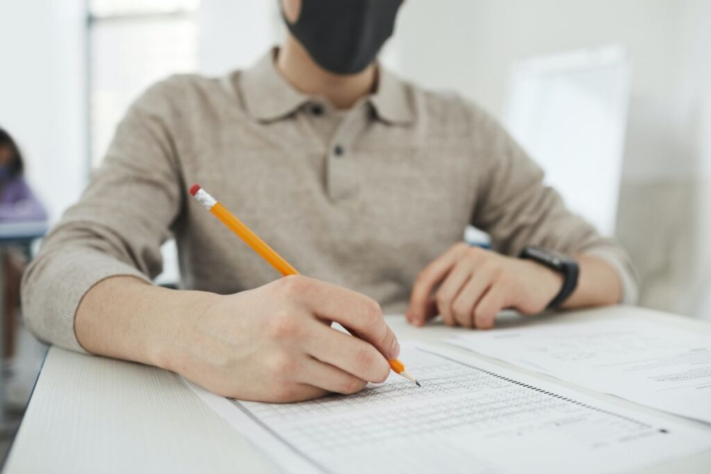 student ce poarta masca cu creionul in mana care sustine examenul Cambridge pe hartie