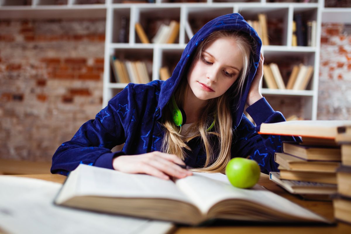 tanara imbracata in hanorac albastru de catifea care studiaza la biroul ei si invata vocabular de incepatori in limba engleza