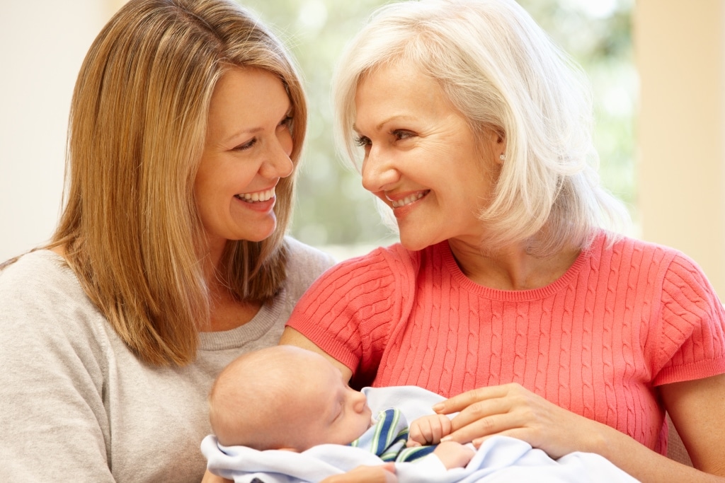 mama si bunica blonde care zambesc cu un bebelus nou-nascut tinut in brate de bunica