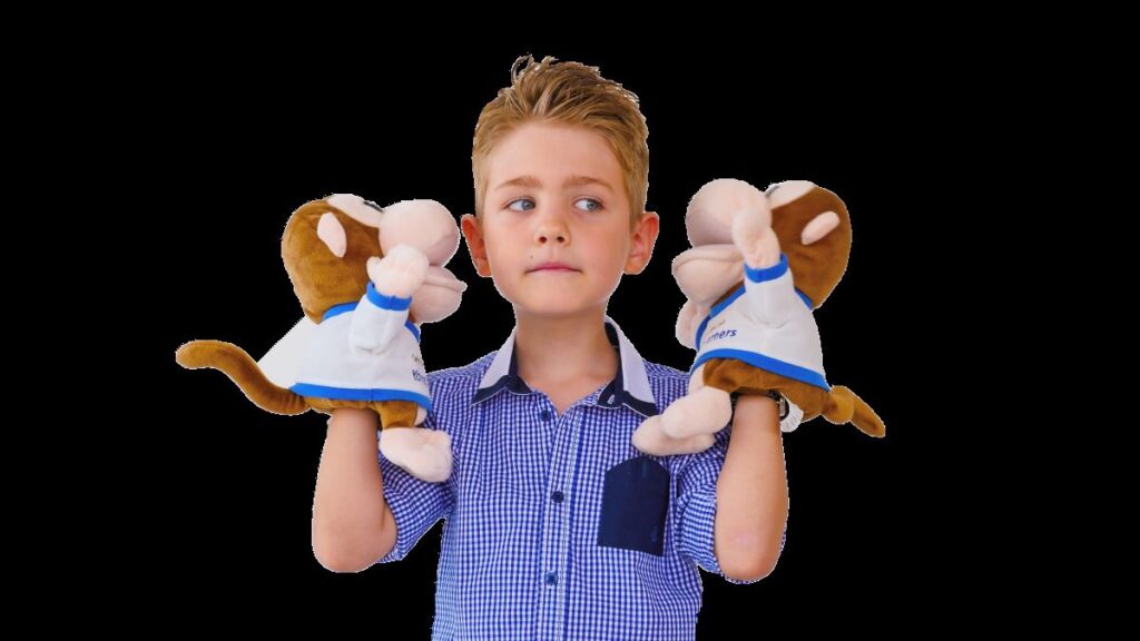 baietel blond in camasa cu carouri albastre tinen in maini marionetele mascota pentru examenul cambridge YLE