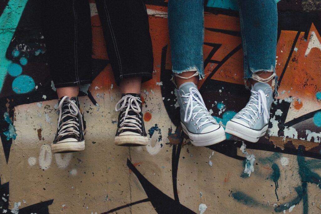 picioare de copii adolescenti imbracati in blugi care stau pe un zid de beton incaltati in pantofi sport de panza