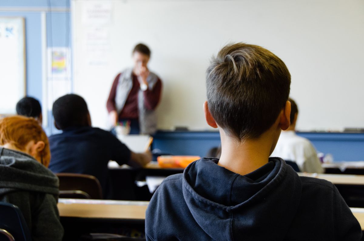 sala de clasa in care se vad din spate cativa elevi asezati in banci si in fata lor profesorul de engleza