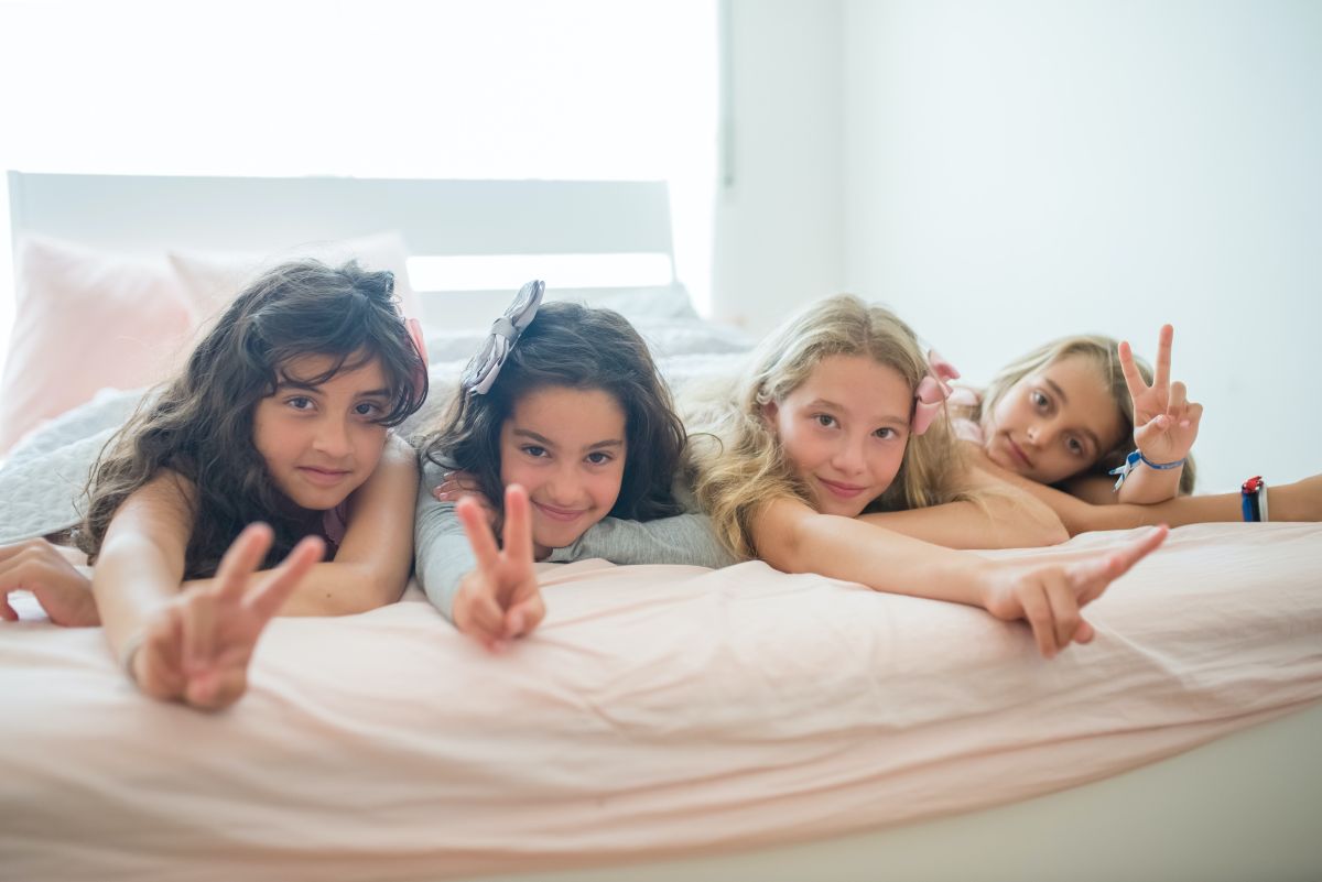 patru fete de gimnaziu stau intinse pe pat si arata semnul de victorie cu degetele dupa ce si-au terminat temele la engleza