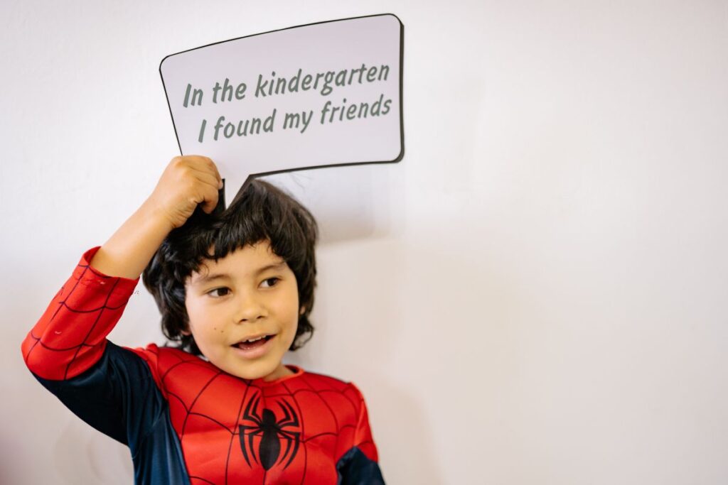baietel prescolar brunet imbracat in costum de spiderman care tine in mana o pancarta pe care scrie In gradinita mi-am gasit prietenii