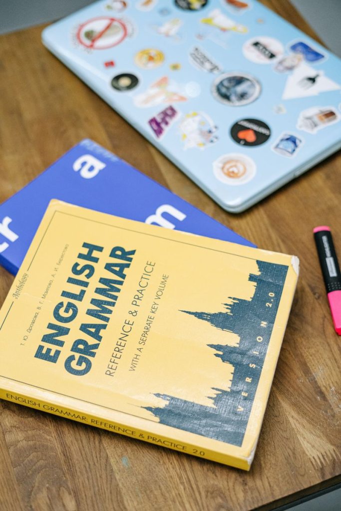 carte de gramatica engleza pe un birou langa doua agende si un evidentiaotor roz