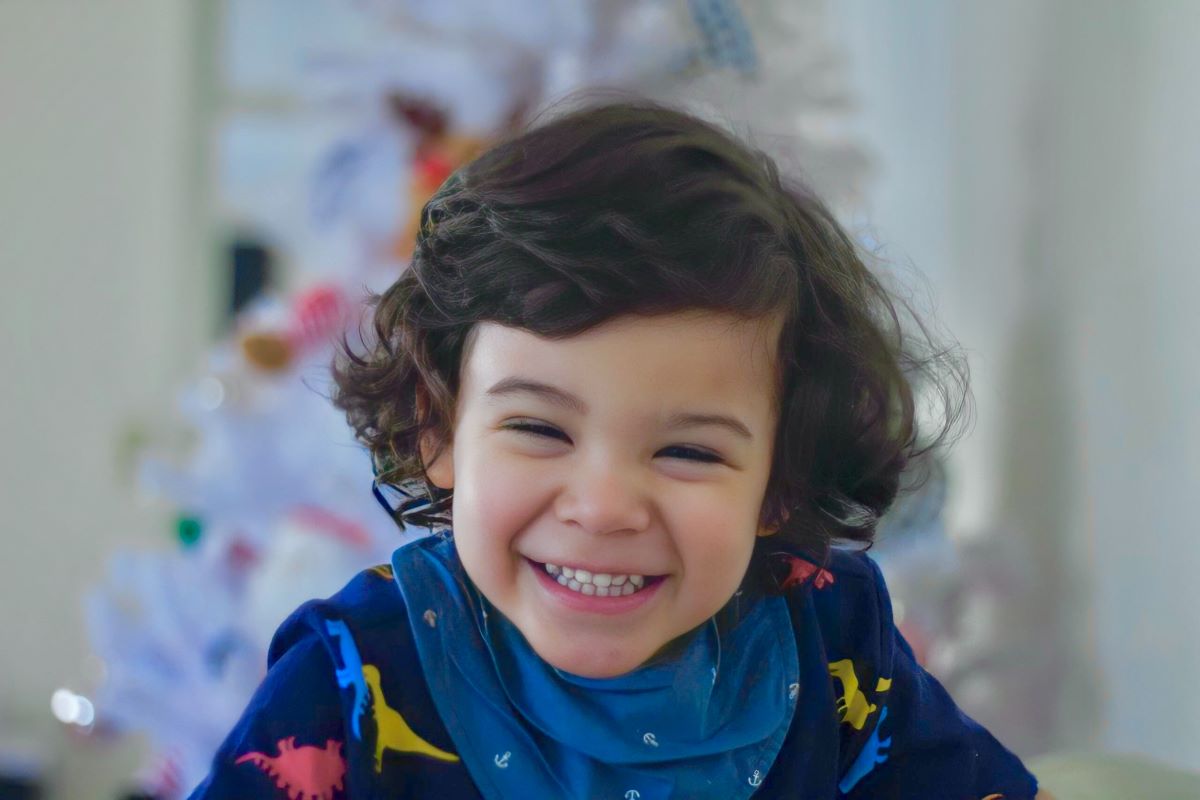 copil de trei ani brunet care zambeste imbracat in albastru