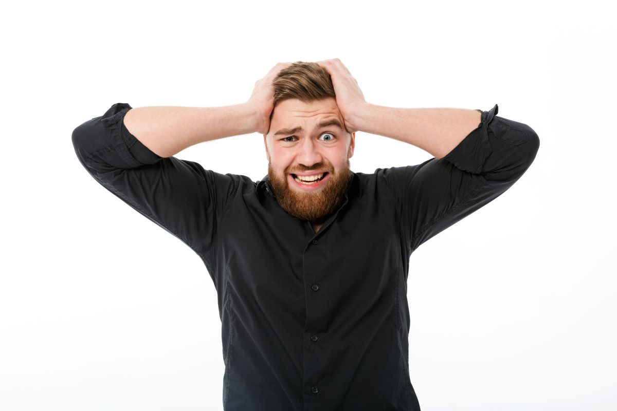 barbat saten cu barba imbracat in camasa neagra se tine cu mainile de cap deoarece nu se pricepe sa spuna cuvinte greu de pronuntat in engleza