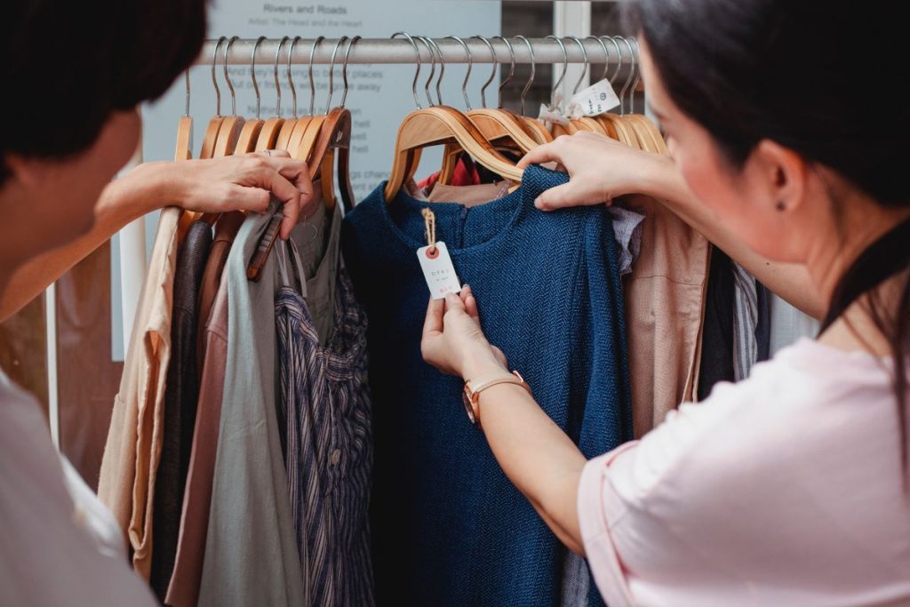 doua femei filmate din spate fac cumparaturi de haine intr-un magazin si compara materialele