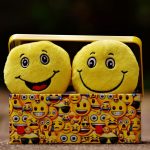 doua perne sub forma de emoji galbene fericite asezate intr-o cutie de carton cu desen cu multe tipuri de emoji