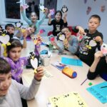 grup de copii in sala de clasa la cursul de engleza zambesc fericiti cu proiectul lor pinguin in mana