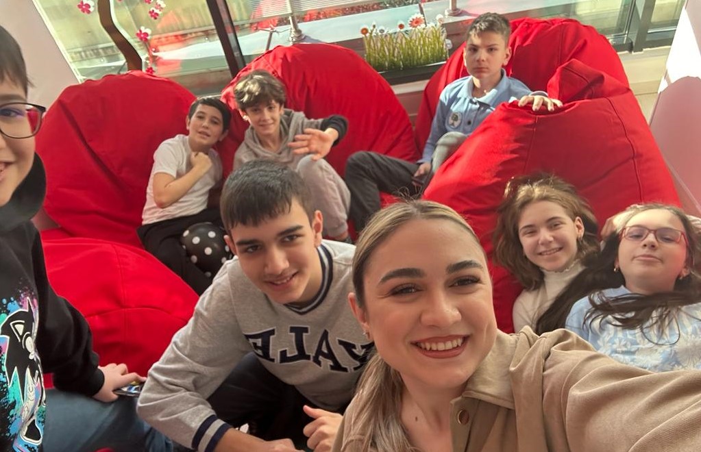 Cursanti FollowMe stand pe fotolii rosii alaturi de unul dintre profesorii scolii de engleza