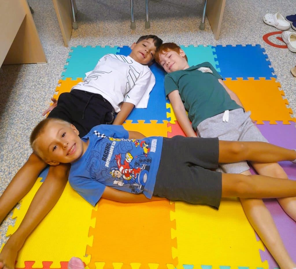 trei copii alcatuiesc cu corpurile lor pe podea litera A