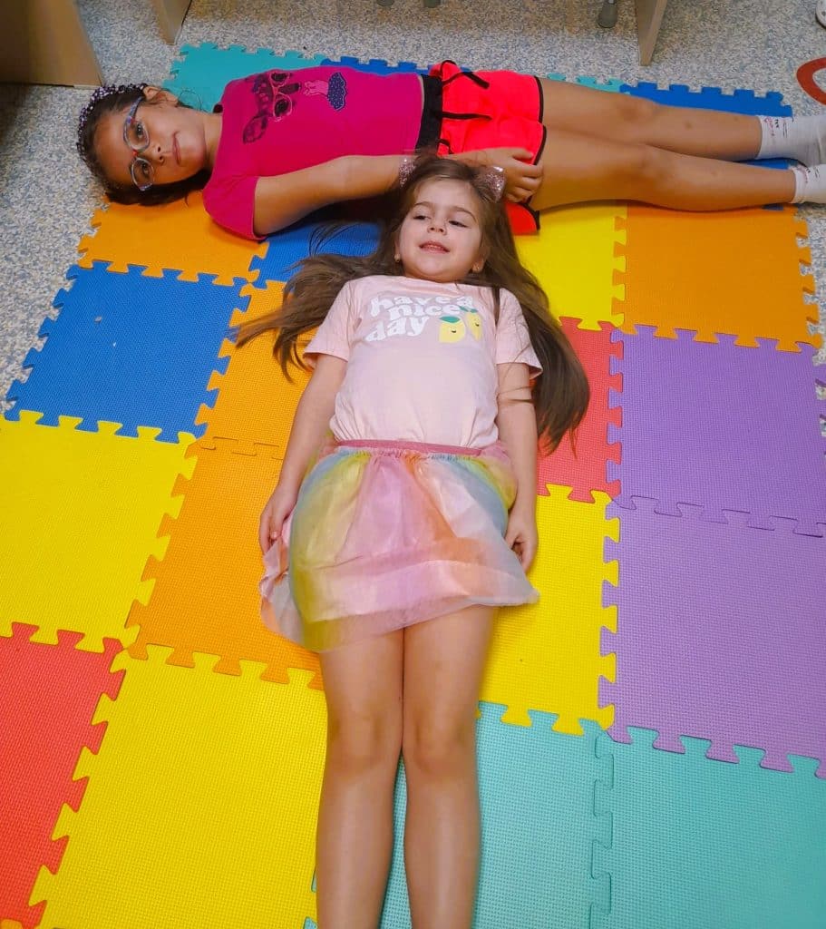 doua fetite realizeaza litera T din corpurile lor pe podea