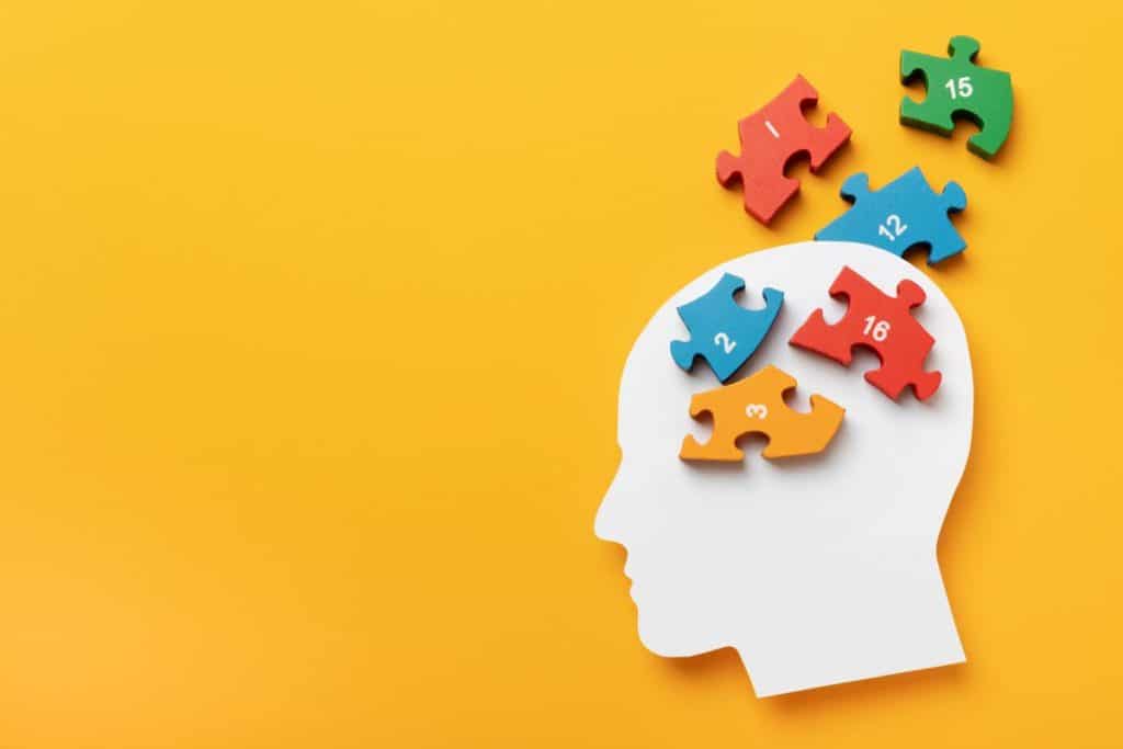 contur de cap alb pe fundal galben cu piese de puzzle colorate ce trebuie aranjate in locul creierului