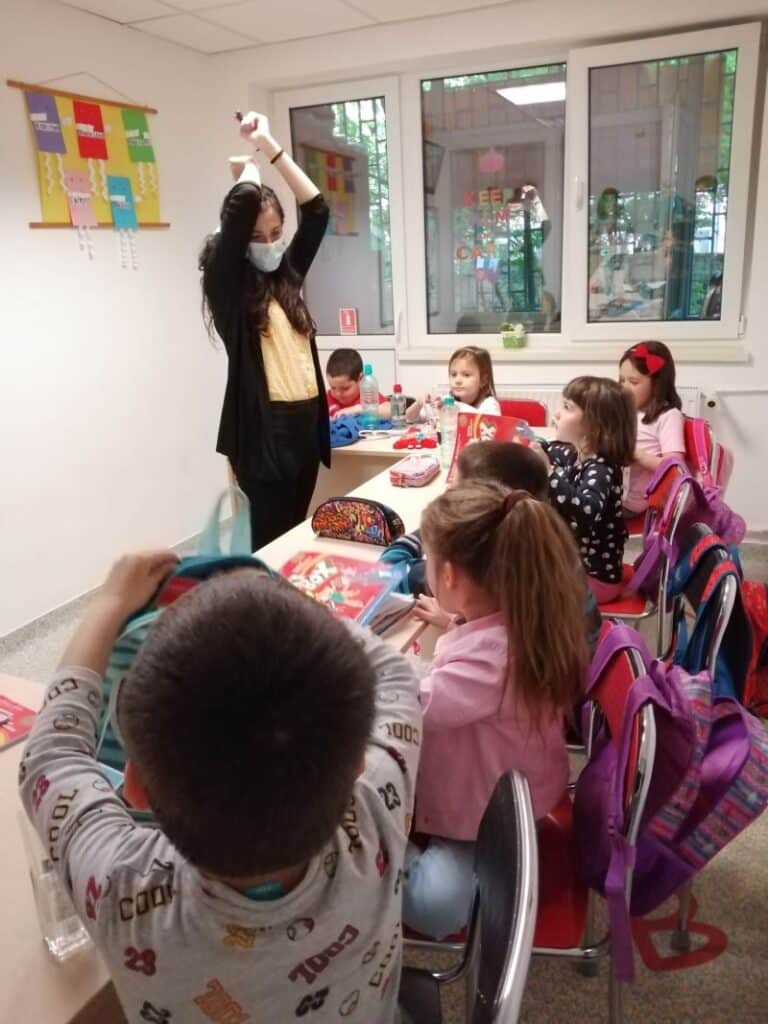 grupe de copii de clasa 0 in sala de clasa alaturi de profesoara lor asculta o poveste audio si o privesc pe aceasta