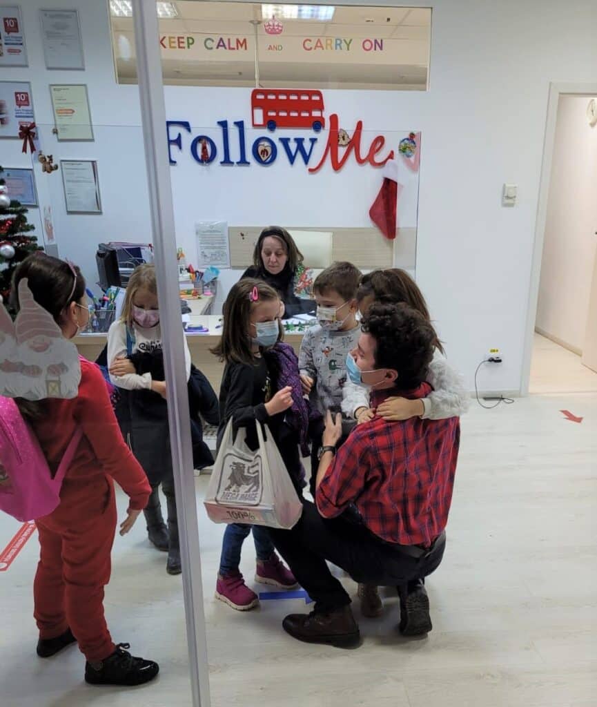 copii prescolari care vin la scoala followme si il imbratiseaza pe profesorul lor de engleza
