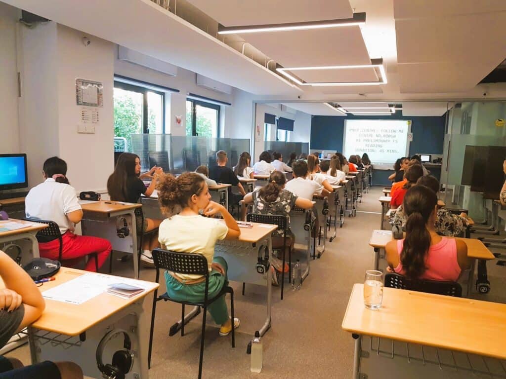 copii fotografiati din spate aflati in sala de examen la testul Cambridge, proba de reading
