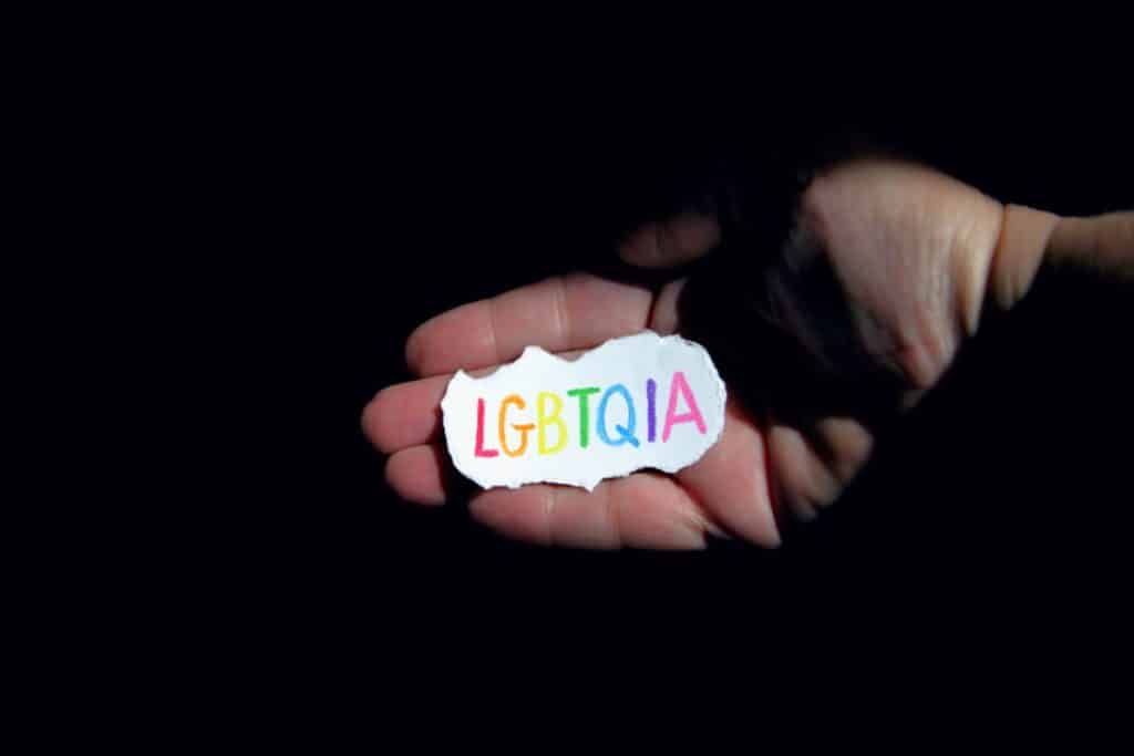 palma pe fundal negru in care e un bilet de hartie alba pe care scrie lgbtqia