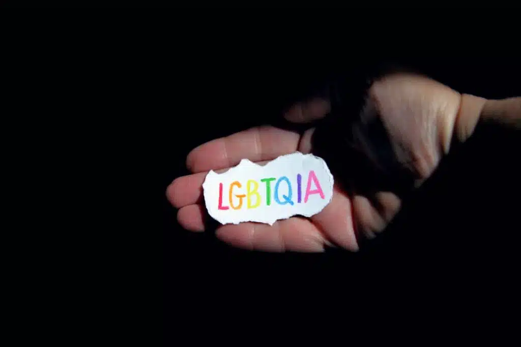 palma pe fundal negru in care e un bilet de hartie alba pe care scrie lgbtqia