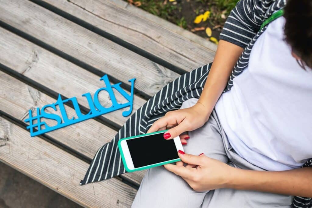 tors si maini de femeie cu unghii rosii ce tine in mana un telefon si se pregateste sa deschida o aplicatie pentru a invata engleza