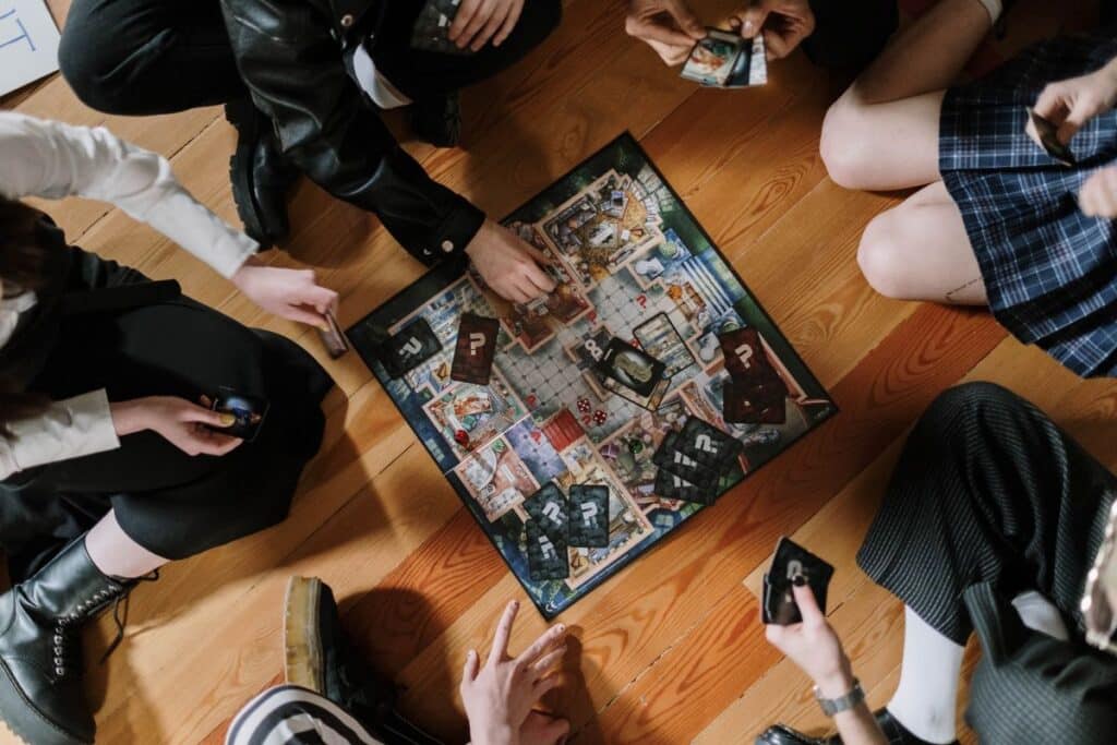 grup de adolescenti ce stau pe o podea de lemn in cerc si joaca un boardgame cu intriga politista si de mister