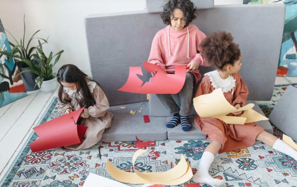 doua fete si un baiat de scoala primara lucreaza impreuna la un proiect decupand forme din cartoane colorate